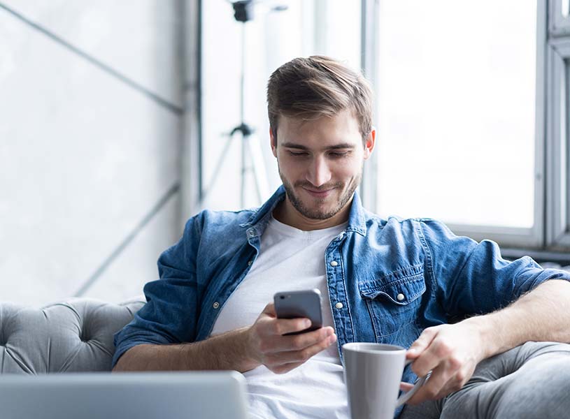 A young man using a smartphone with drinking coffee in his home
