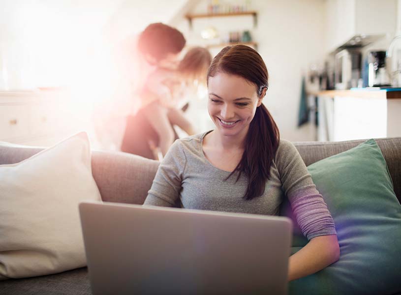 A young lady using a laptop computer in her home with her family behind her